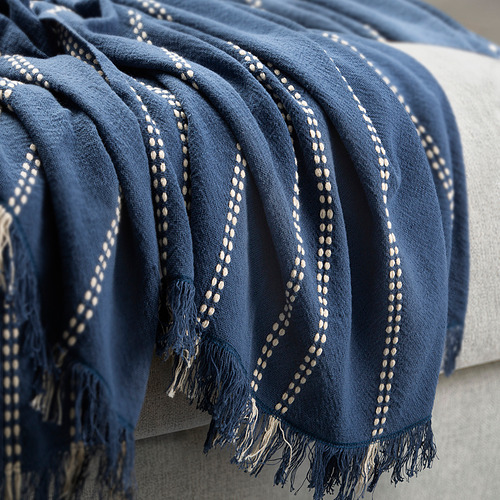 Elegante manta azul con tejido dobby a rayas, extremos con flecos, drapeado sobre el sofá.