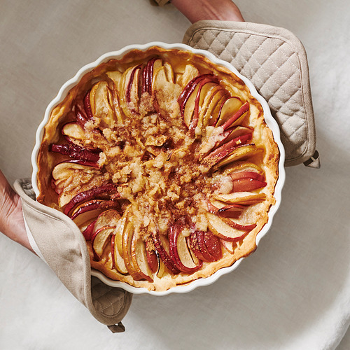 Manos sosteniendo guantes de cocina con tarta de manzana al horno.