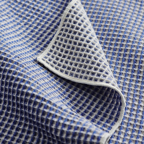 Toalla de tejido de gofre azul y blanco doblada, que muestra intrincados patrones de diamantes, con una apariencia suave y texturizada.