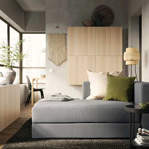 Sala de estar moderna con sofá JÄTTEBO gris, almohadas verdes, arte de pared tejido, gabinete de madera y ventana grande.