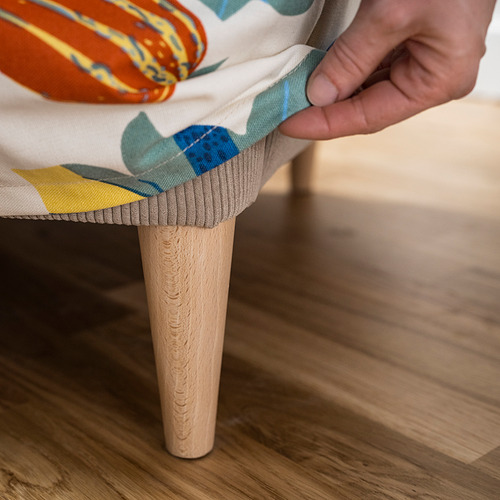 Persona ajustando un cojín elegante y colorido sobre patas de madera.