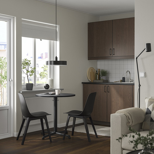 Cocina moderna con armarios de madera oscura, juego de comedor negro junto a la ventana, lámpara colgante, sala de estar con sofá y lámpara, decoración minimalista con plantas.