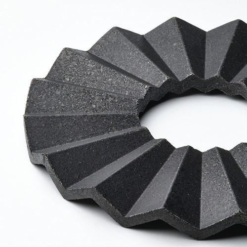 Un salvamanteles negro y circular con segmentos angulares y superpuestos, elaborado en bambú comprimido, que emana una estética moderna y una calidad robusta.
