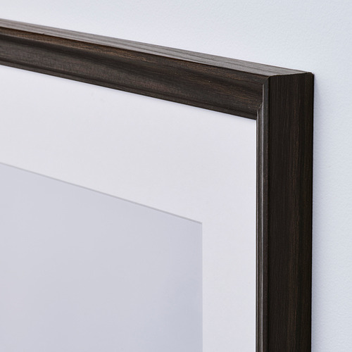 Marco de madera oscura con cubierta de plástico transparente, apoyado contra la pared blanca.