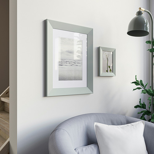 Habitación minimalista con marco gris, foto de playa, sillón azul, hojas verdes, lámpara negra.
