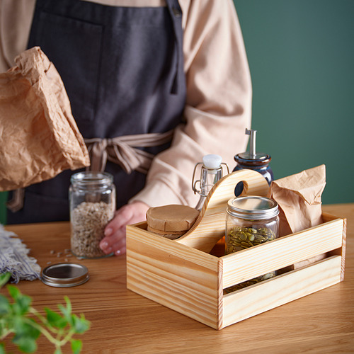 Una persona que sostiene una caja de madera llena de frascos de semillas y botellas, probablemente relacionada con la jardinería o el cultivo de plantas.