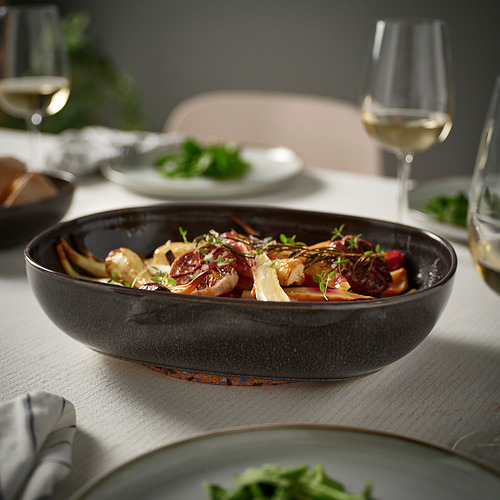 Plato de horno GLADELIG gris oscuro lleno de comida en una mesa de comedor, acompañado de copas de vino y platos con verduras, que sirven varias porciones.