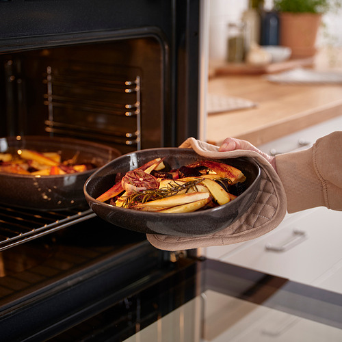 Persona colocando una fuente de horno gris oscuro llena de verduras asadas en un horno abierto.