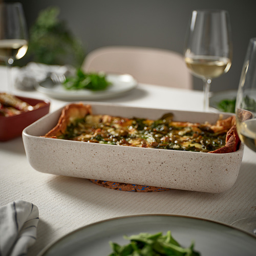 Plato de horno LYCKAD beige con comida, copas de vino y platos sobre una mesa.