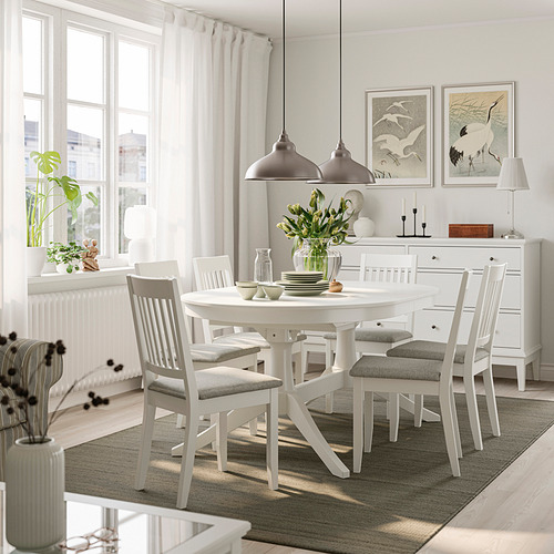 Juego de comedor ROSENTORP con mesa extensible y sillas acolchadas de color gris, bajo luces colgantes, junto a un gran ventanal y aparador decorado.