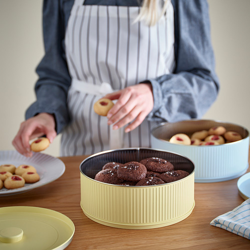 Persona sosteniendo una galleta, rodeada de recipientes de productos horneados. Cuencos y platos rellenos de galletas sobre mesa de madera.