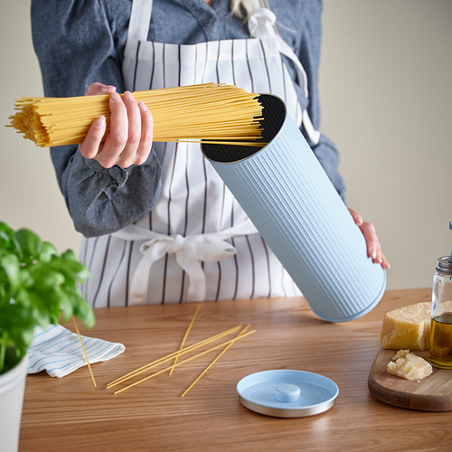 Persona sosteniendo un dispositivo BETTHAJ azul claro con espaguetis adentro, mostrando la escena de la cocina.