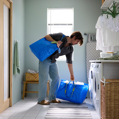 Un hombre manejando grandes bolsos azules de ikea FRAKTA en un lavadero.