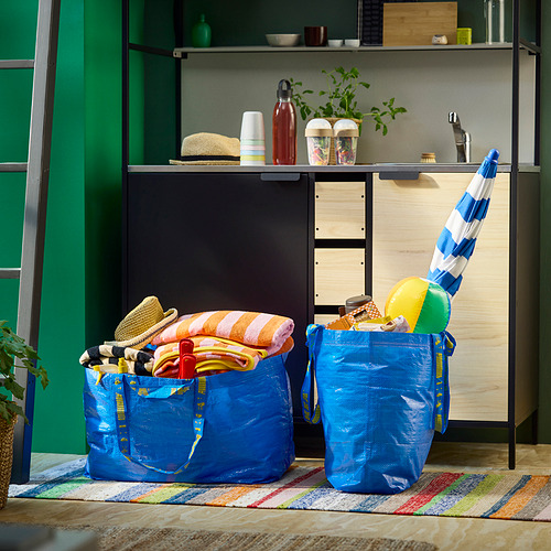 Bolsas azules de IKEA FRAKTA con toallas y juguetes en alfombra de colores cerca de la pared verde.