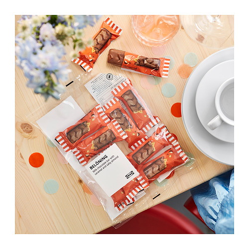 Barras de chocolate abiertas BELÖNING en mesa de madera con copas de vino, plato, taza, flores, confeti.