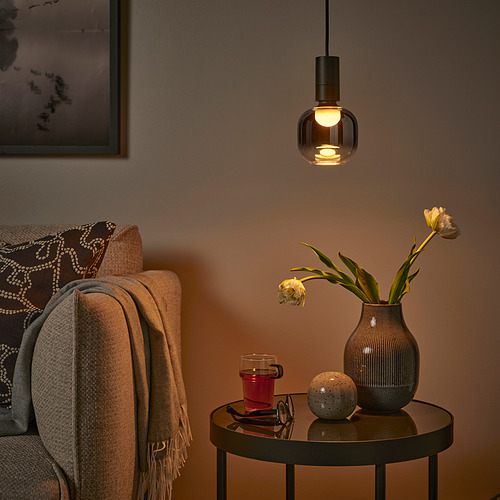 Rincón acogedor con sofá beige, luz MOLNART, flores, taza, esfera, brillo suave y cálido.