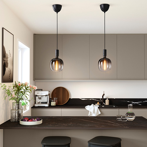 Cocina moderna con lámparas colgantes negras, taburetes, frutas, jarrón. Iluminado por elegantes luces de vidrio, obras de arte, gabinetes en el fondo.