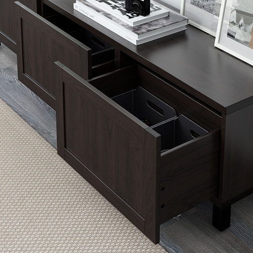 Cómoda BESTÅ de madera oscura con cajones abiertos con función de cierre suave, sobre una alfombra ligera y texturizada.