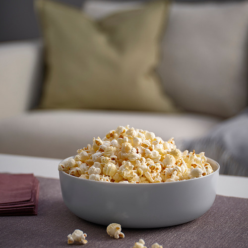 Tazón de palomitas de maíz en el sofá. Cuenco de cristal blanco VITBLECKA, grande, redondo, diseño sencillo. El tazón contiene una cantidad significativa de palomitas de maíz, cerca de servilletas de color burdeos.