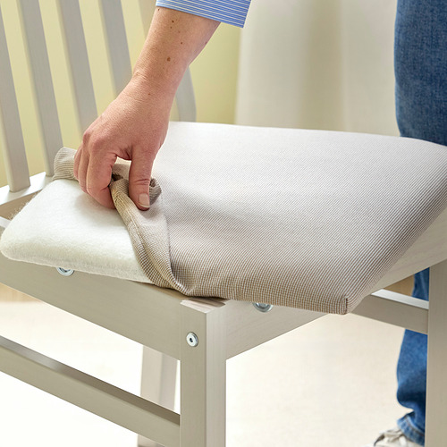 Persona limpiando una silla con un cojín blanco y estructura de madera, utilizando un paño.