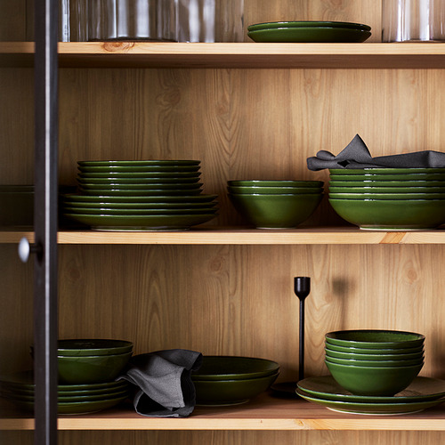 Estantes de platos y cuencos de gres PELARKAKTUS de color verde oscuro, cuidadosamente apilados, de tamaño variado, que contrastan con la madera clara.