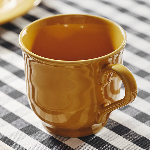 Taza dorada sobre mantel a rayas, superficie lisa, diseño robusto.