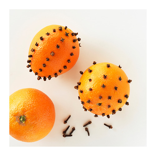 Tres naranjas; dos decoradas con clavo. Una naranja lisa con un tallo verde. Sobre fondo blanco.