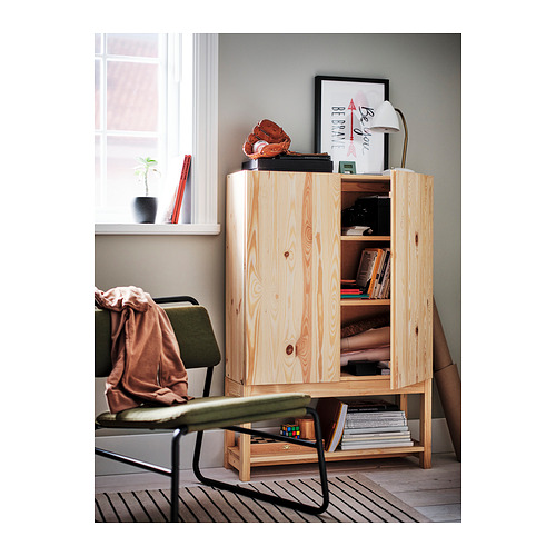 Armario de almacenamiento de madera con estantes abiertos y puertas cerradas, colocado cerca de una ventana. Decorado con una lámpara, marcos y plantas.