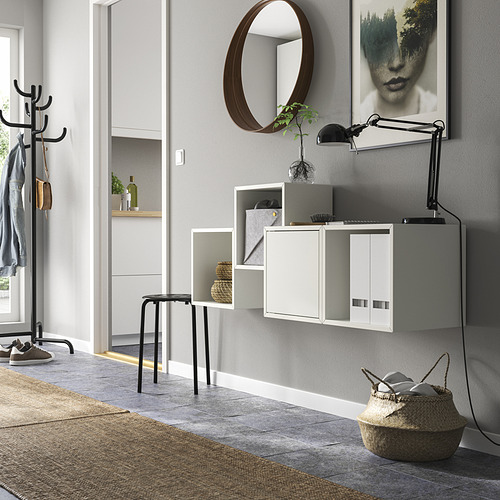 Entrada moderna con muebles de almacenamiento blancos EKET, abrigos colgantes, un espejo redondo y una cesta de mimbre.