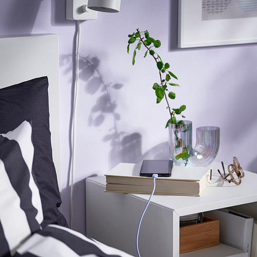 Mesita de noche con cable de carga usb, planta, libro, teléfono y lámpara.