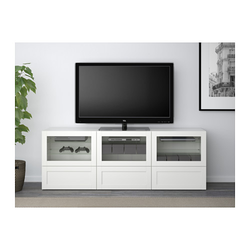 Moderno mueble de TV blanco con puertas de vidrio, que muestra controladores de juegos y dispositivos electrónicos. Incluye gestión de cables y cierre suave.