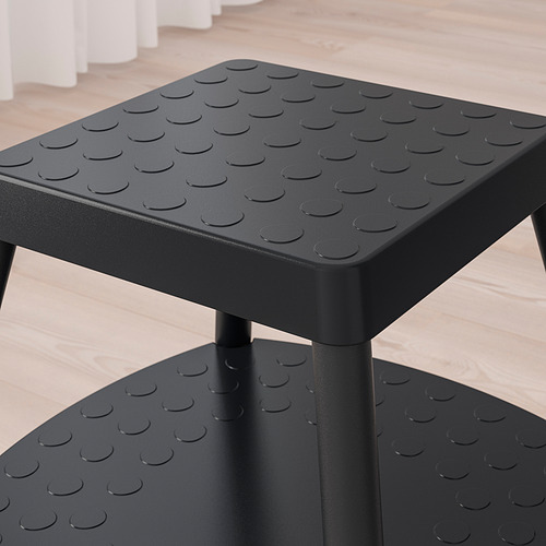 Taburete negro con superficie antideslizante texturizada, patas metálicas resistentes y un estante, diseñado para brindar estabilidad y seguridad.
