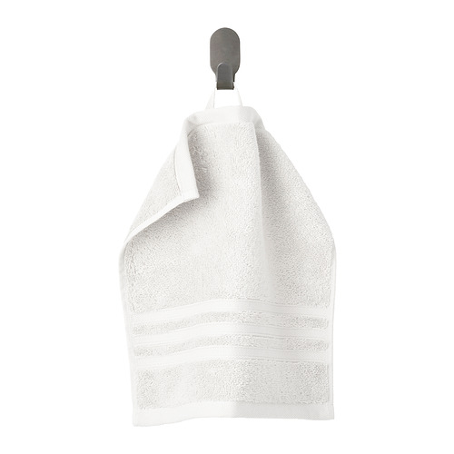 Una toalla blanca de algodón orgánico cuelga de una percha gris, doblada cuidadosamente con un borde tejido.