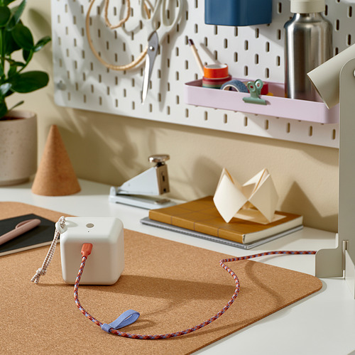 Un colorido cable usb-c en espiral descansa sobre una alfombrilla de corcho, rodeado de suministros de oficina en casa y soluciones de almacenamiento.