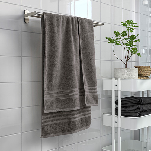 Una toalla gris BROKGLIM sobre una varilla de metal, grande, suave, absorbente, de algodón orgánico con borde tejido en el baño.