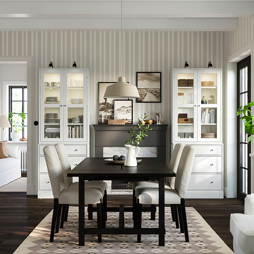 Un comedor con una mesa HAVSTA negra, sillas de colores claros y un armario con frente de cristal.