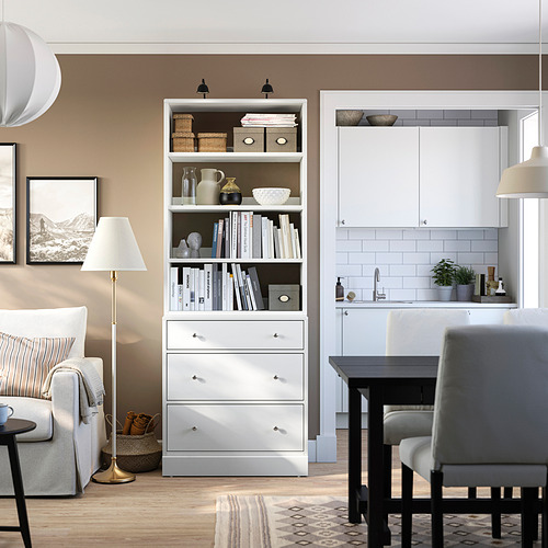 Sala de estar moderna con unidad de almacenamiento HAVSTA. Cajones y estantes blancos entre el sofá y la cocina. Alfombra decorada y elegante.