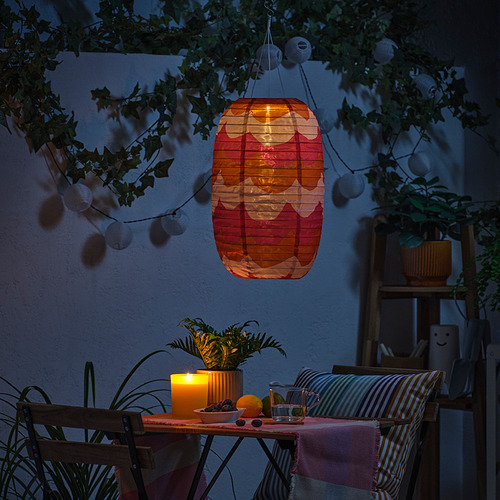 Patio nocturno con linterna, velas, plantas, sillas y luces de cadena.