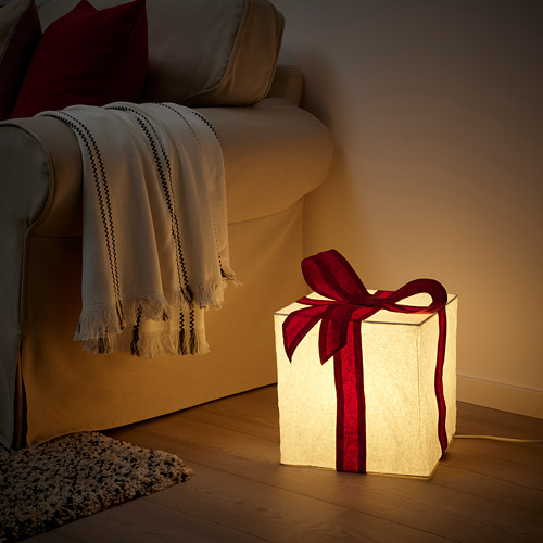 Lámpara STRÅLA de Ikea: brillante, cuadrada, papel blanco con cinta roja. Se sienta en el suelo junto a una silla acogedora.