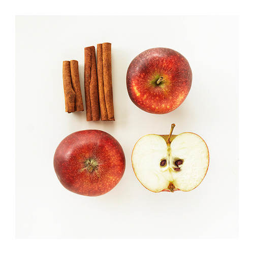 Cuatro manzanas dispuestas en un cuadrado, dos manzanas rojas enteras, una manzana cortada con semillas, con tres ramas de canela