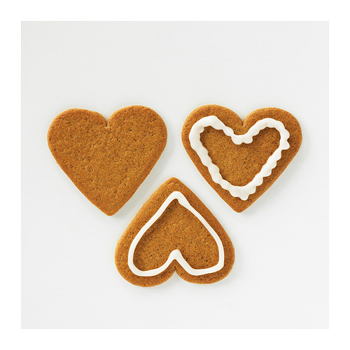 Tres galletas de jengibre en forma de corazón, dos con bordes de glaseado blanco sobre superficie blanca.