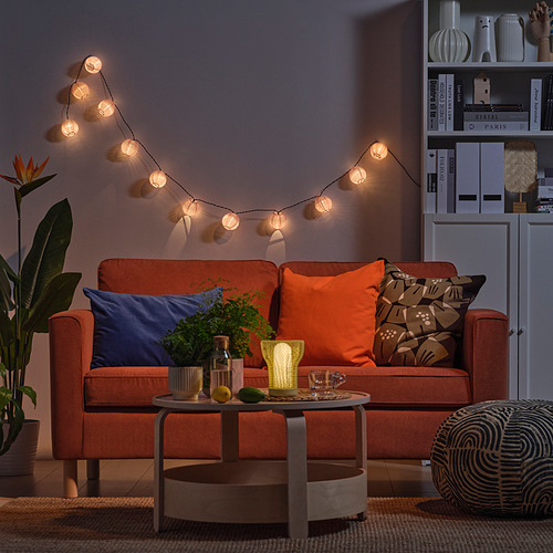 Acogedora sala de estar con sofá naranja, guirnaldas de luces, mesa de café, decoración de limón y planta.