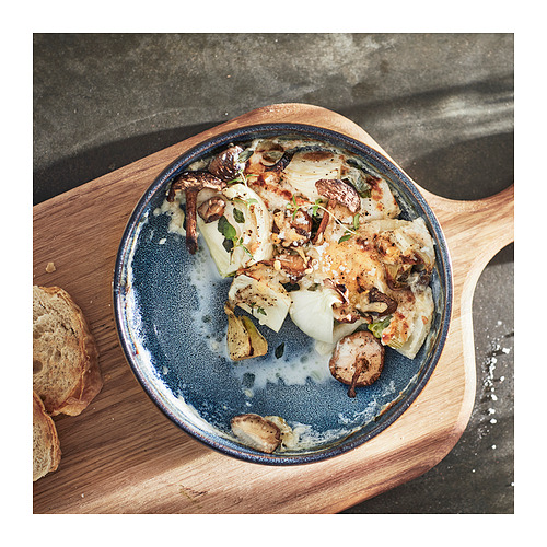Plato ovalado de gres vidriado azul, relleno de verduras asadas y champiñones, colocado sobre una tabla de madera con rebanadas de pan.