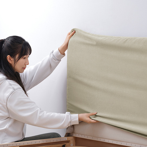 Una mujer asegura una funda de cama beige texturizada. Se encaja en el marco de la cama con facilidad.