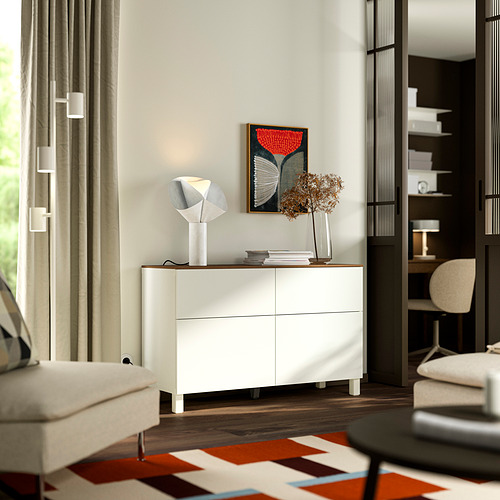 Moderna sala de estar con aparador, lámpara y flores BESTÅ . Sillón blanco, alfombra colorida.