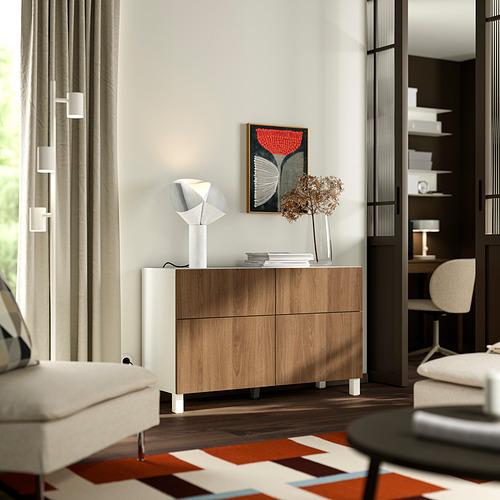 Habitación minimalista moderna con aparador BESTÅ , lámpara, flores secas, alfombra, sillón, ventana y estantería.