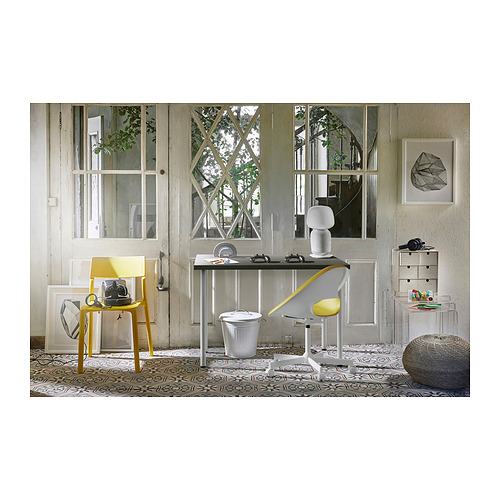 Moderna configuración de oficina con mesa y silla LINNMON amarilla, ventana grande, escritorio con computadora portátil y cajón de almacenamiento.