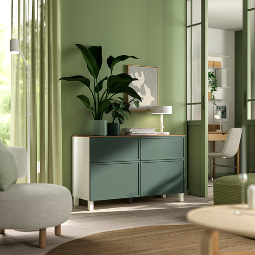 Sala de estar moderna con aparador BESTÅ verde claro, planta, libros, lámpara y silla gris.