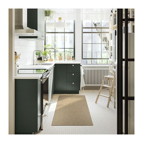 Cocina moderna con alfombra beige LÄTTBETONG, armarios de color verde oscuro, azulejos blancos y taburetes de madera junto a una gran ventana.