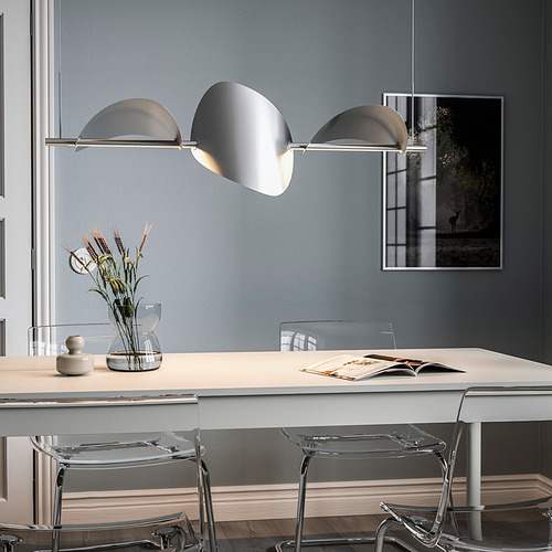Moderna lámpara BACKSTÖRN sobre mesa de comedor, que ilumina libros y flores.